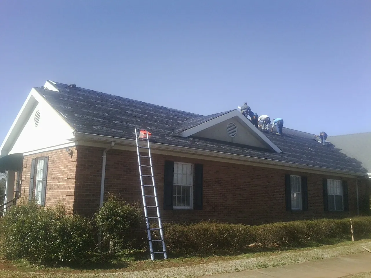 Crew tearing shingles off a brick ranch roof with a ladder set — Emergency Roof Repair work by our crew in Uncasville