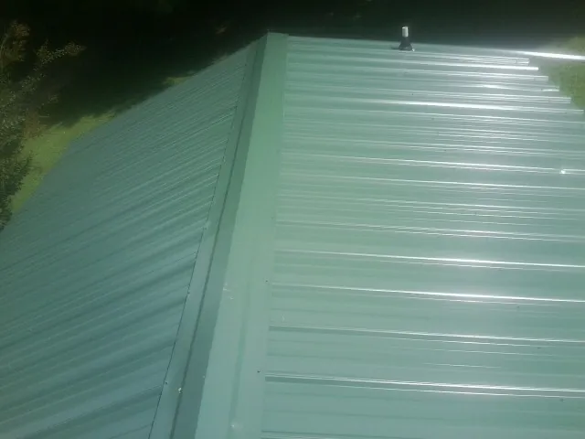New green metal panels meeting at the ridge of a roof — Flat Roof Repair work by our crew in Uncasville