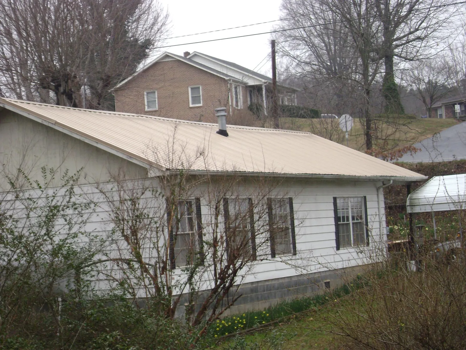 Tan metal roof on a white sided house set into a hillside — Commercial Roofing by Roofing Brothers in Uncasville